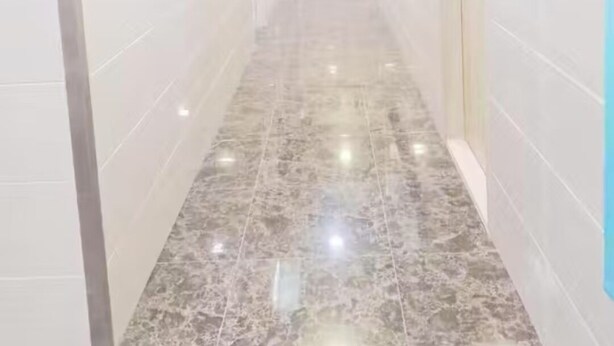 A hallway with white tiled walls and a marble floor, leading to a room with a bed and a window. - Nanqiang Hostel (Kowloon)
