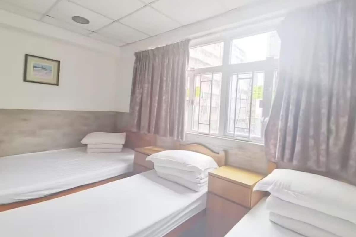 A hotel room with two single beds, a wooden headboard, a window with curtains, and a framed picture on the wall.