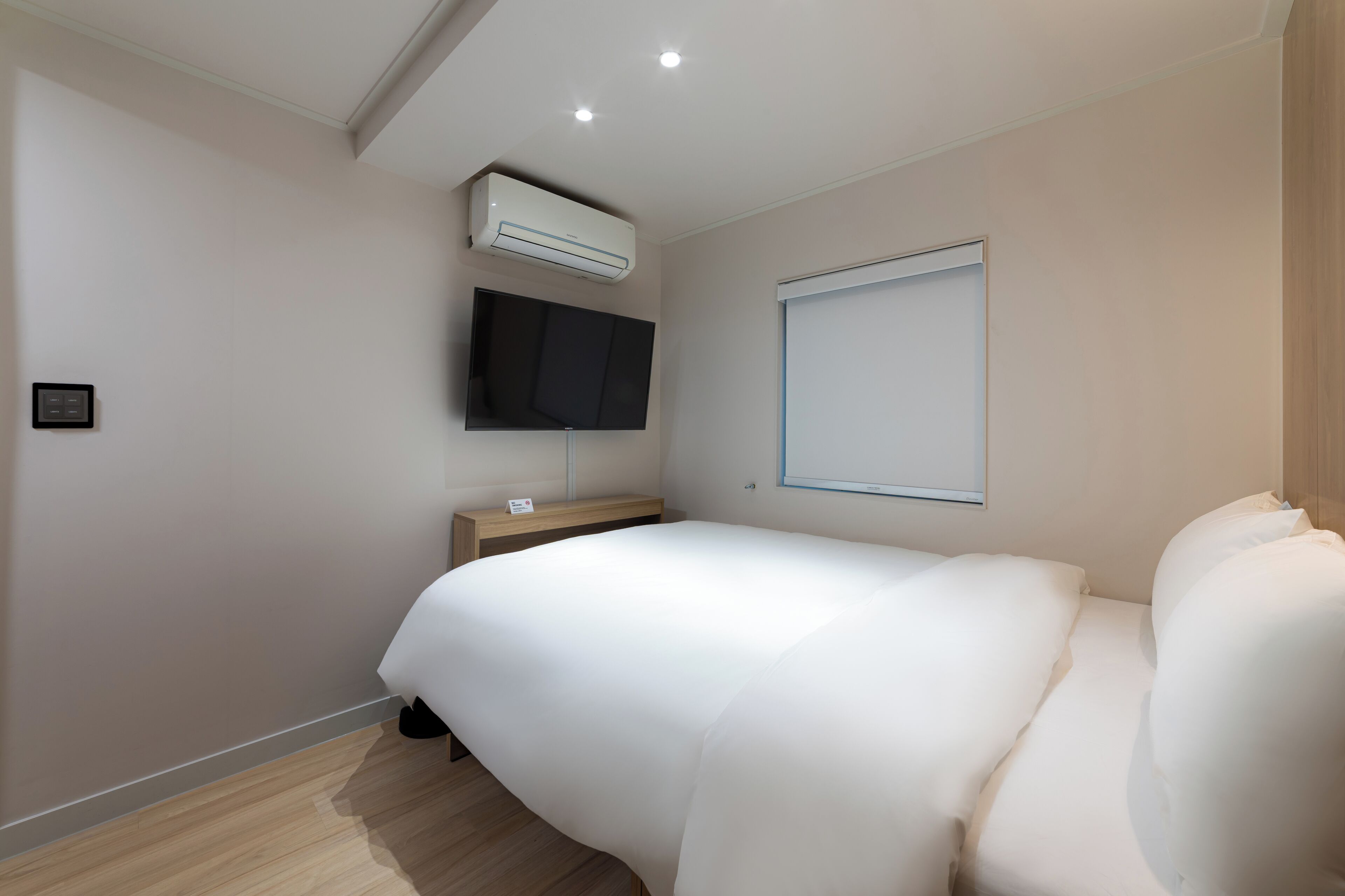 Une chambre d’hôtel moderne dotée d’un grand lit, d’un téléviseur à écran plat fixé au mur et d’un appareil de climatisation placé au-dessus.