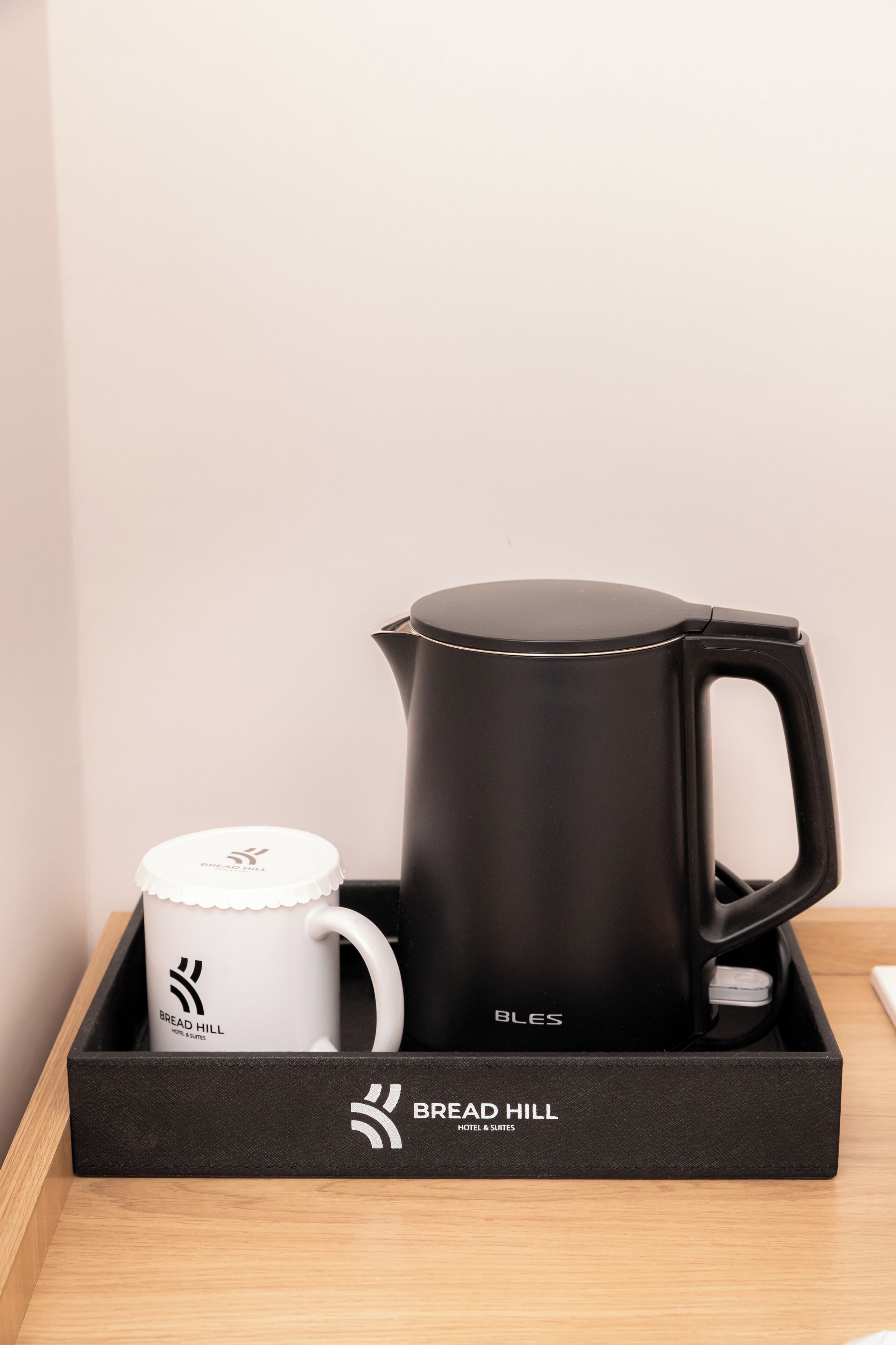 Una bandeja negra con una cafetera y una taza blanca sobre una superficie de madera.