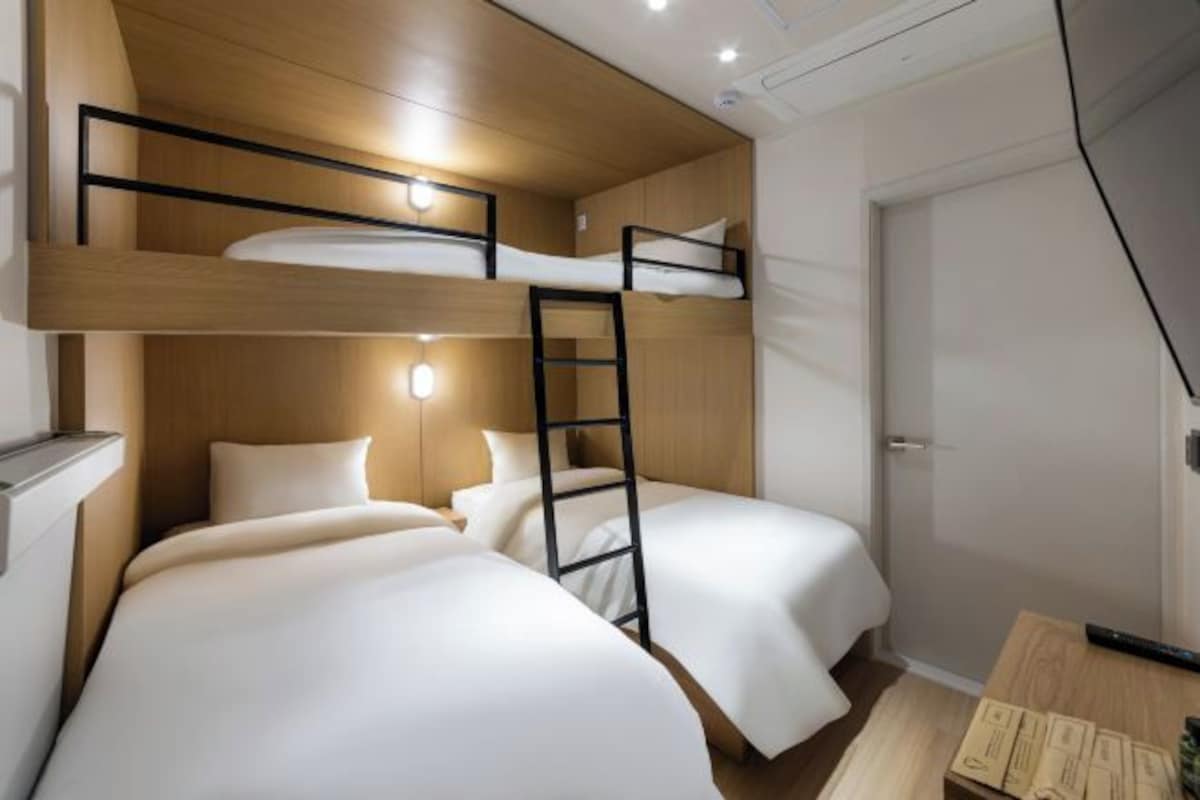 Habitación con literas, dos camas, una escalera y una mesita con objetos encima.