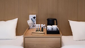 Ein Hotelzimmer mit zwei Betten, einem Holzkopfende, einem Nachttisch mit Lampe, einer Kaffeemaschine und einem gerahmten Bild.