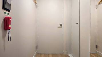 A hallway with a wooden floor, a fire alarm, a coat hook, and a door.