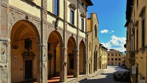 Calle con edificios históricos, paseos con arcos y mesas al aire libre.