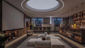 Una sala de estar moderna con una lámpara de techo circular, una zona de bar con estantes llenos de botellas y un área de descanso con sofás y una mesa de centro.
