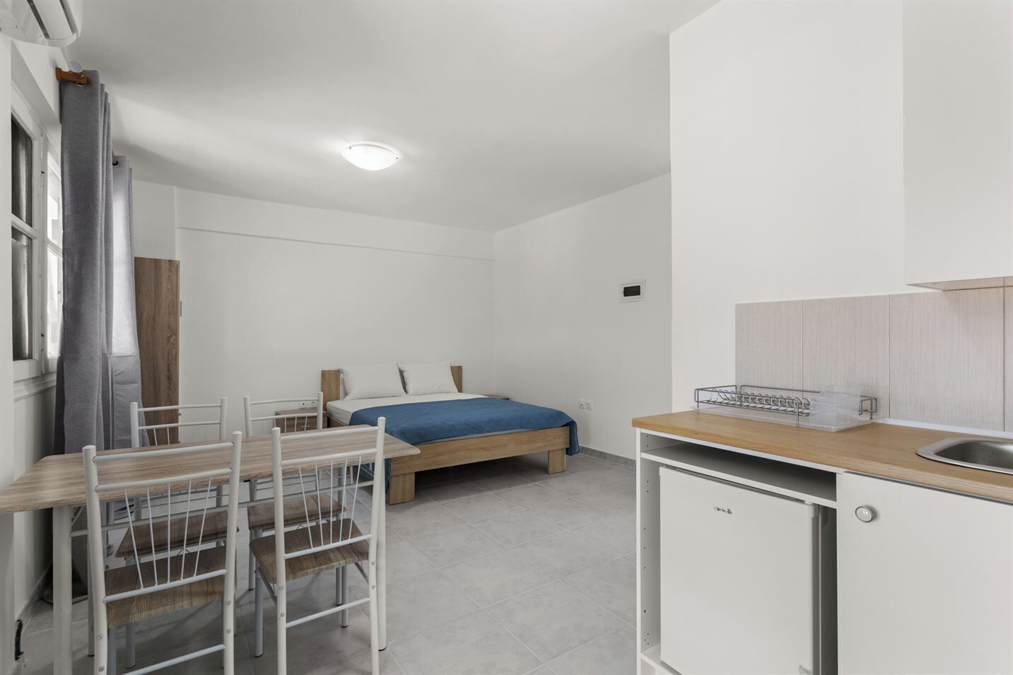 A compact room with a bed, a small dining table, and a kitchenette.