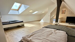 Een moderne loft slaapkamer met dakraam, een bed, bureau en televisie.