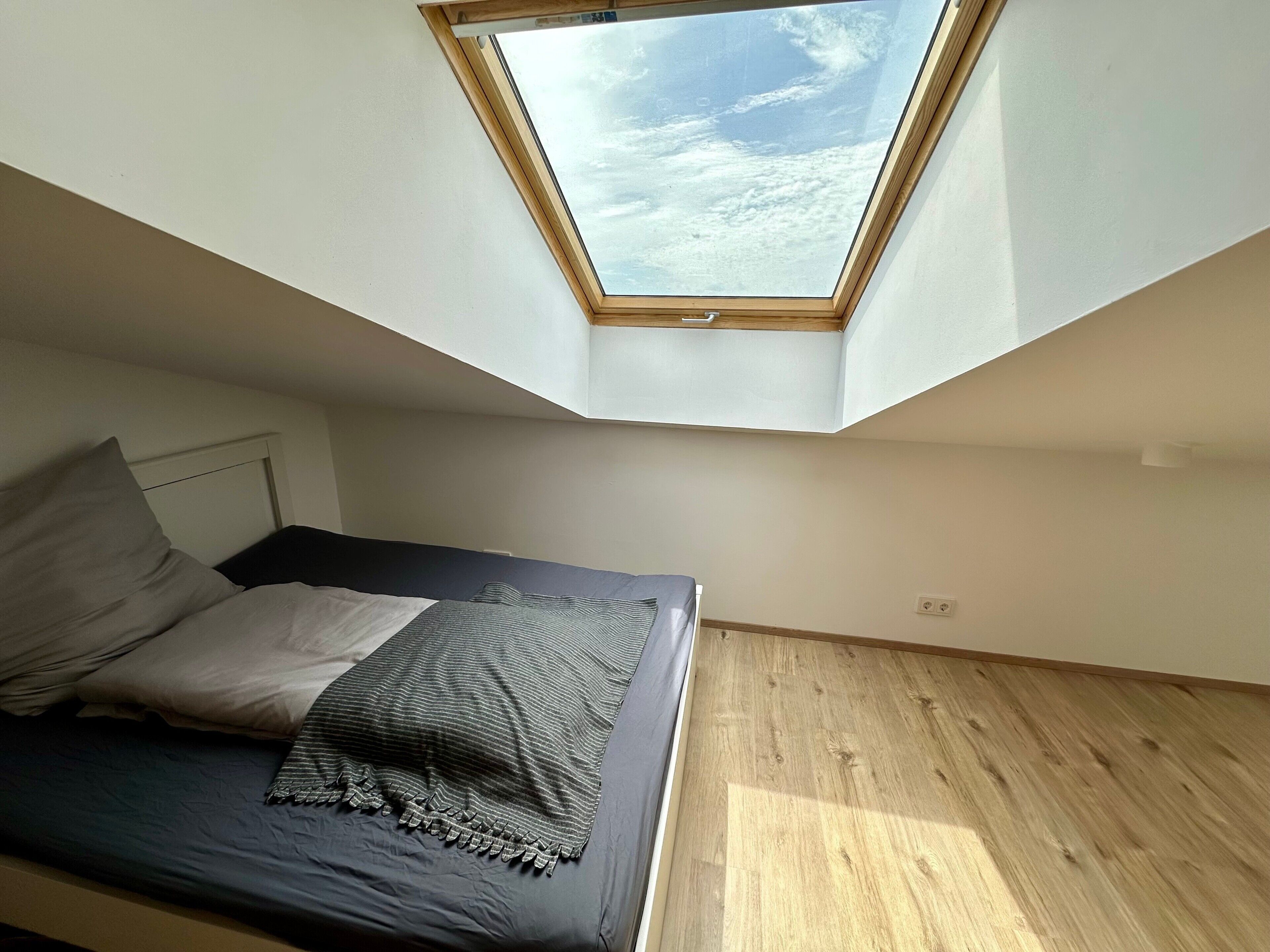 Ein Schlafzimmer mit Dachfenster, einem Bett mit Kissen und Holzboden.