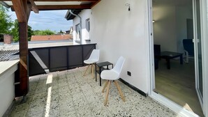 Een overdekt balkon met een tafel en stoelen, een schuifdeur naar een kamer binnen en uitzicht op de omgeving.