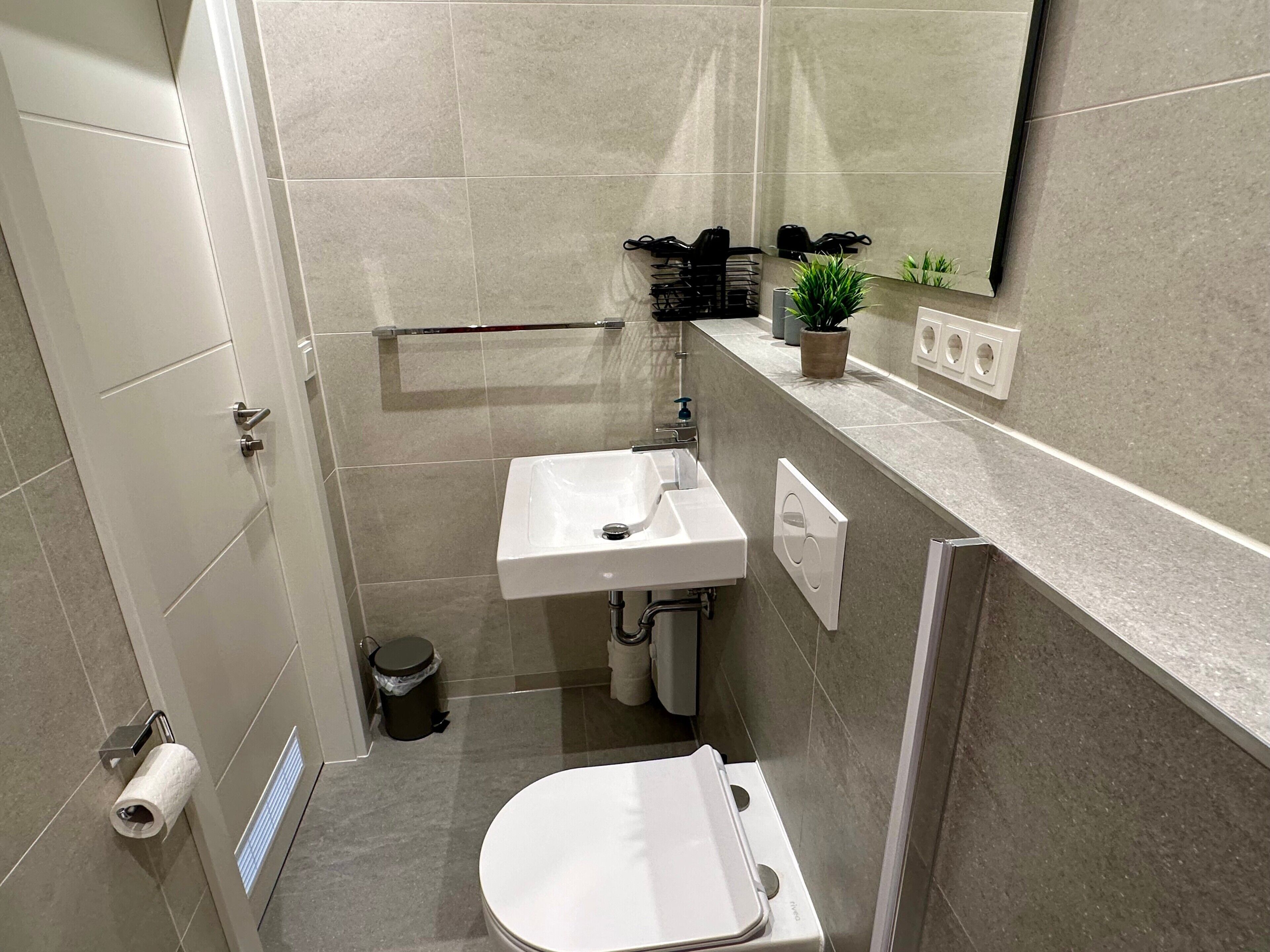 Ein kleines Badezimmer mit einem weißen Waschbecken, einer Toilette und einem Spiegel über dem Waschbecken.