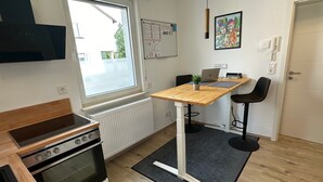 Een kleine keuken met een inbouwoven, een raam, een whiteboard en een laptop op een houten tafel.