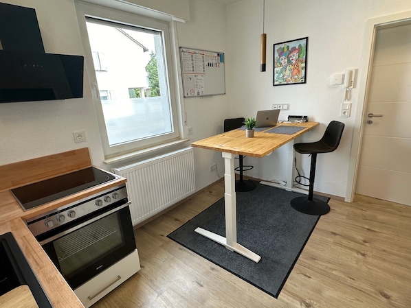 A compact kitchen with a built-in oven, a window, a whiteboard, and a laptop on a wooden table.