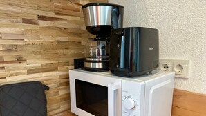 Een compacte magnetron met een koffiezetapparaat erboven, een stopcontact en een zwarte tas op de vloer.