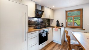 Een moderne keuken met witte kasten, een zwarte oven, een houten aanrecht en een raam met uitzicht op groen.
