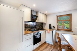 A modern kitchen with white cabinets, a black oven, a wooden countertop, and a window with a view of greenery. - Holiday Home with Private Terrace (Wolfach-Kirnbach)