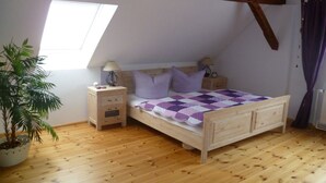 Een slaapkamer met schuine plafond, een houten bed, twee nachtkastjes met lampen, een kamerplant en een raam.
