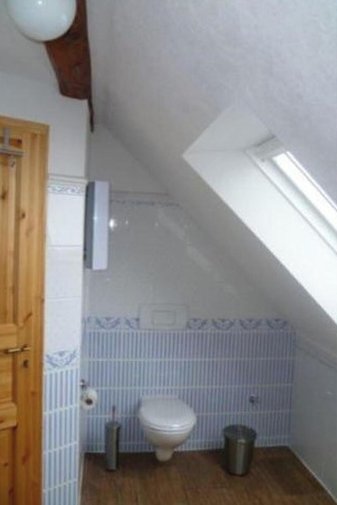 Un baño pequeño con inodoro, bidé, cubo de basura y puerta de madera.