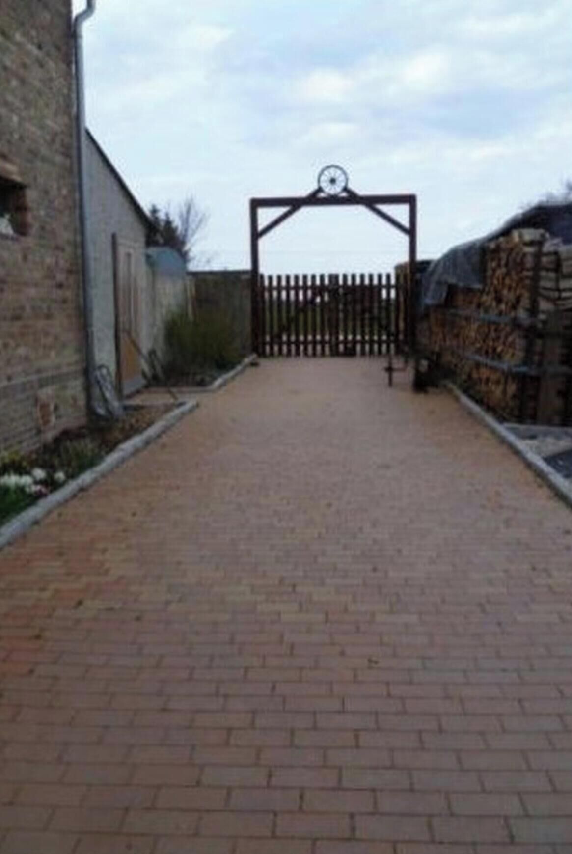 A paved pathway leading to a gated entrance with a metal gate and a clock above it.