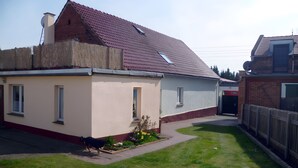 Een gelijkvloers huis met schuin dak, een kleine tuin en een houten hek.