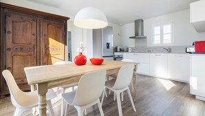 Une cuisine moderne avec des meubles blancs, une table à manger en bois et un grand luminaire suspendu.