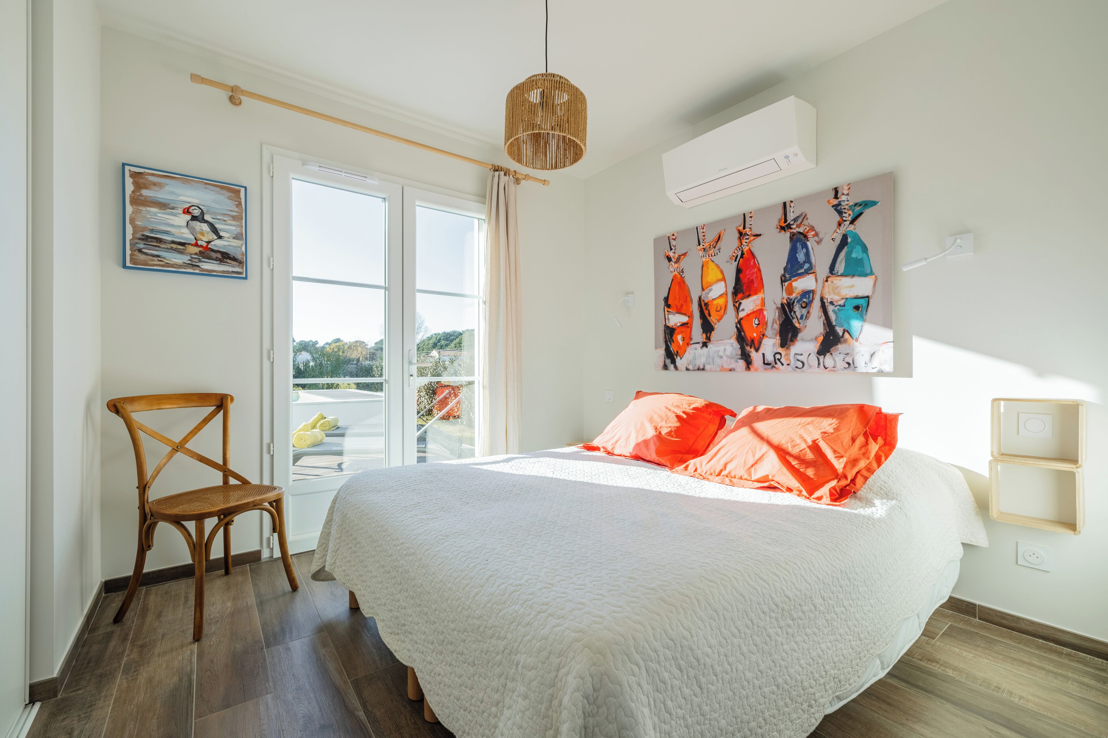 Een slaapkamer met een groot bed, een houten stoel, een schilderij van vissen en een airconditioning.