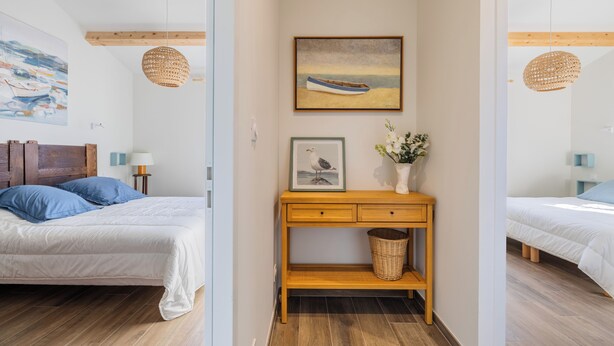Un dormitorio con cabecera de madera, una mesita de noche con lámpara, un cuadro enmarco y una cesta de mimbre.