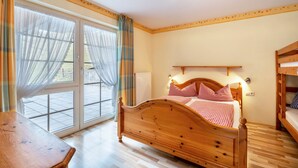 A bedroom with a wooden bed, a bedside table, a window with curtains, and a bunk bed in the corner. - Holiday Apartment 'Waldblick' with Shared Pool and Large Terrace (Wolfach-Kirnbach)
