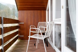 A balcony with a wooden railing, a white metal chair, and a window with a white curtain. - Studio Room 'Courtyard View Without Kitchen' with Balcony (Wolfach-Kirnbach)