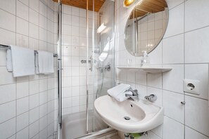 A bathroom with a glass shower enclosure, a sink with a mirror above it, and a towel rack with two towels. - Studio Room 'Courtyard View Without Kitchen' with Balcony (Wolfach-Kirnbach)