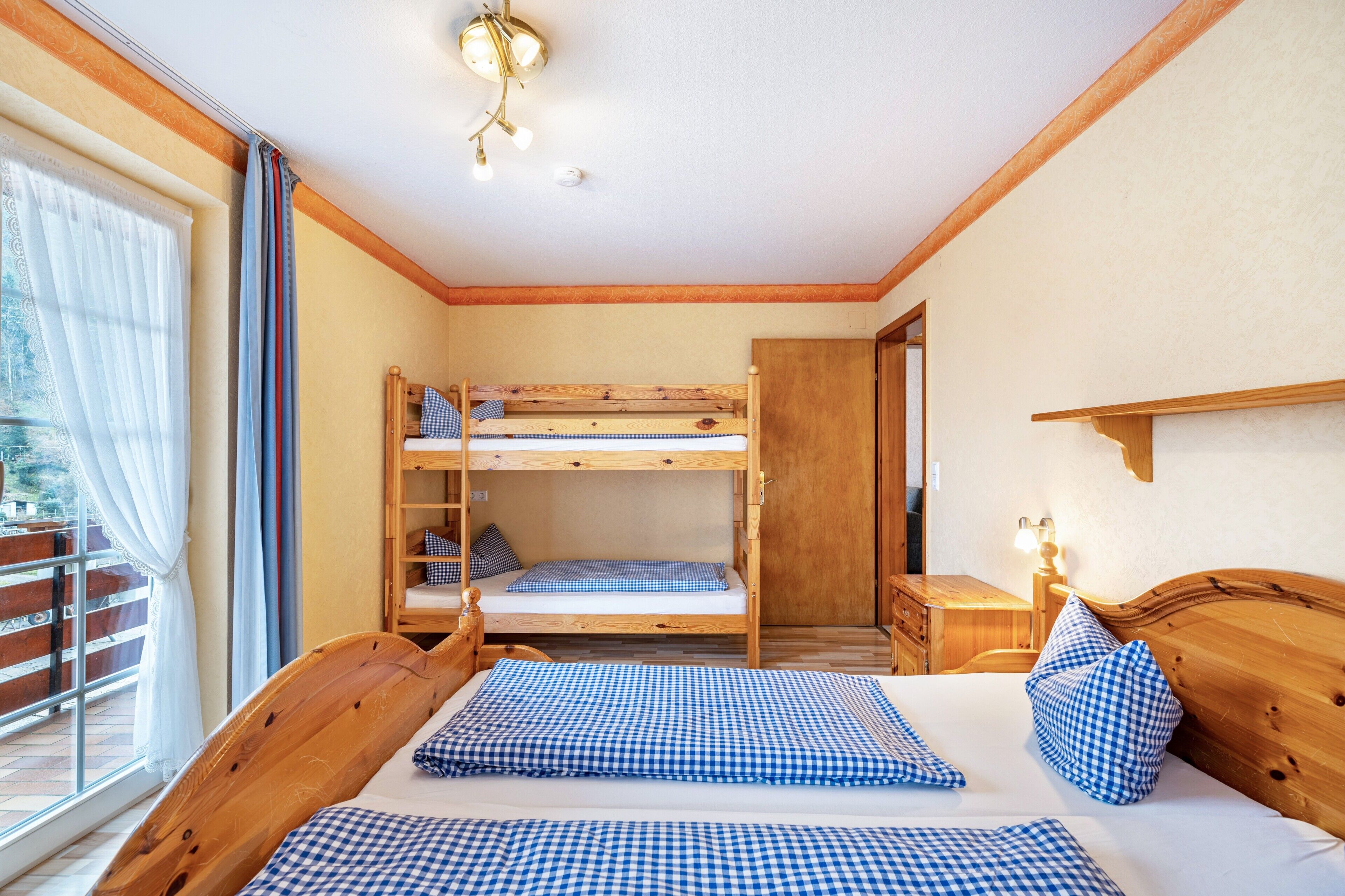 Une chambre avec un lit superposé, un bureau en bois, une chaise et une fenêtre avec des rideaux.
