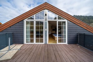 A modern house with a sloped roof, large glass doors leading to a wooden interior, and a deck area. - Holiday Apartment 'Bergblick' with Balcony (Wolfach-Kirnbach)