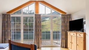 A room with a large sliding glass door, a television on a wooden cabinet, and a wooden ceiling. - Holiday Apartment 'Bergblick' with Balcony (Wolfach-Kirnbach)