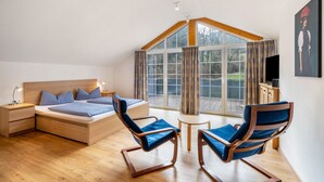 A bedroom with a bed, two chairs, a small table, a nightstand, and a TV. - Holiday Apartment 'Bergblick' with Balcony (Wolfach-Kirnbach)