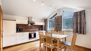 A modern kitchen with wooden flooring, a dining table with chairs, and a large window with curtains. - Holiday Apartment 'Bergblick' with Balcony (Wolfach-Kirnbach)