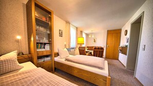 A hotel room with two beds, a wooden bookshelf, a dining table with chairs, and a lamp. - Apartment 'Kaltenbach' with Shared Terrace, Shared Garden and Wi-Fi (Schonach)