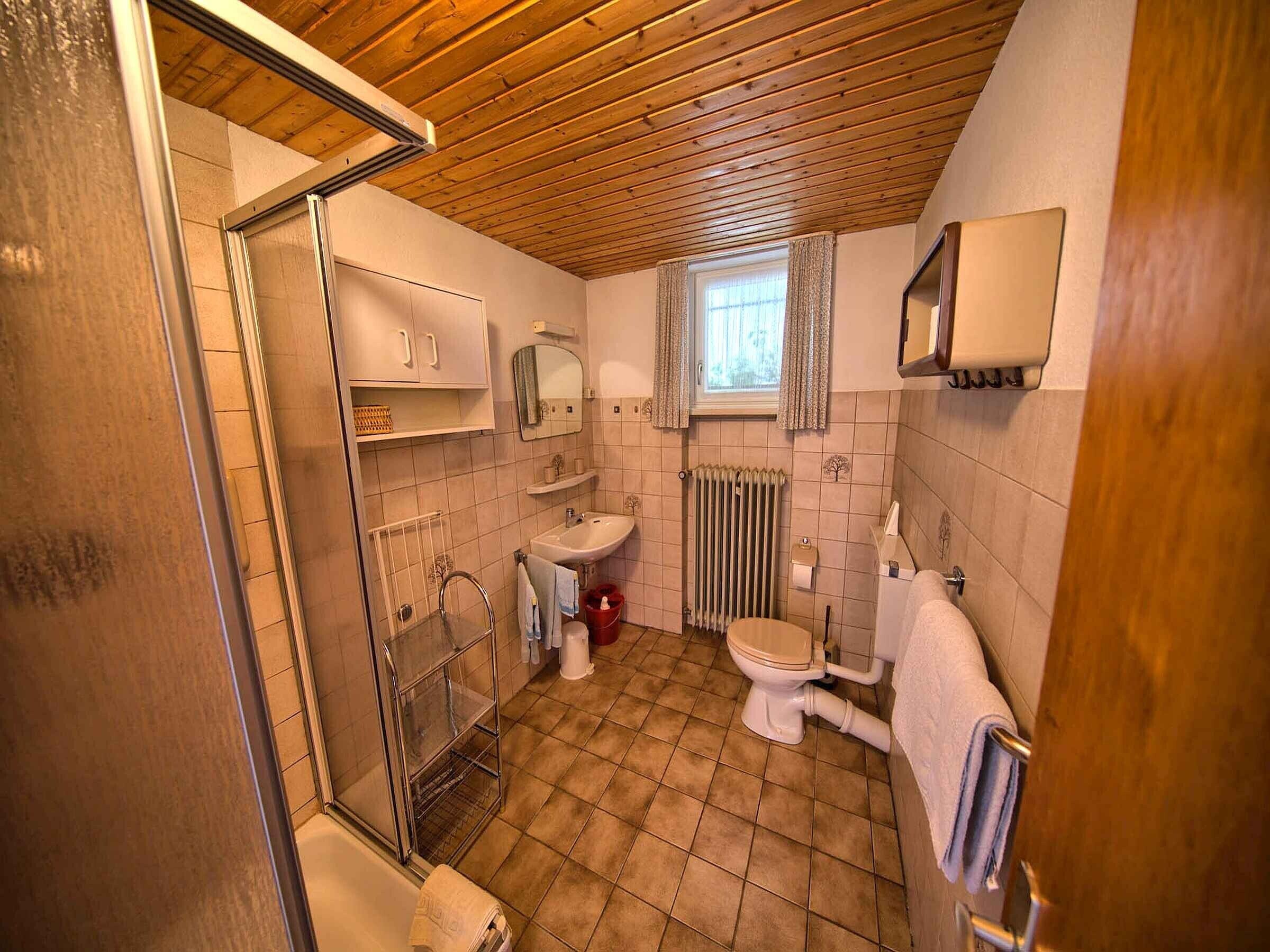 A bathroom with a shower, toilet, sink, and a window with curtains.