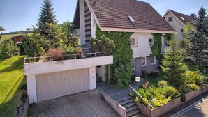 A two-story residential building with a sloped roof, a garage, and a small front garden with steps leading to the entrance. - Apartment 'Kaltenbach' with Shared Terrace, Shared Garden and Wi-Fi (Schonach)