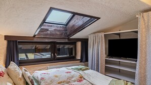 Un dormitorio con tragaluz, una cama con ropa de cama floral, un televisor y un armario.