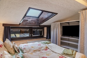 Une chambre avec un puits de lumière, un lit avec une literie à motifs floraux, une télévision et une armoire.