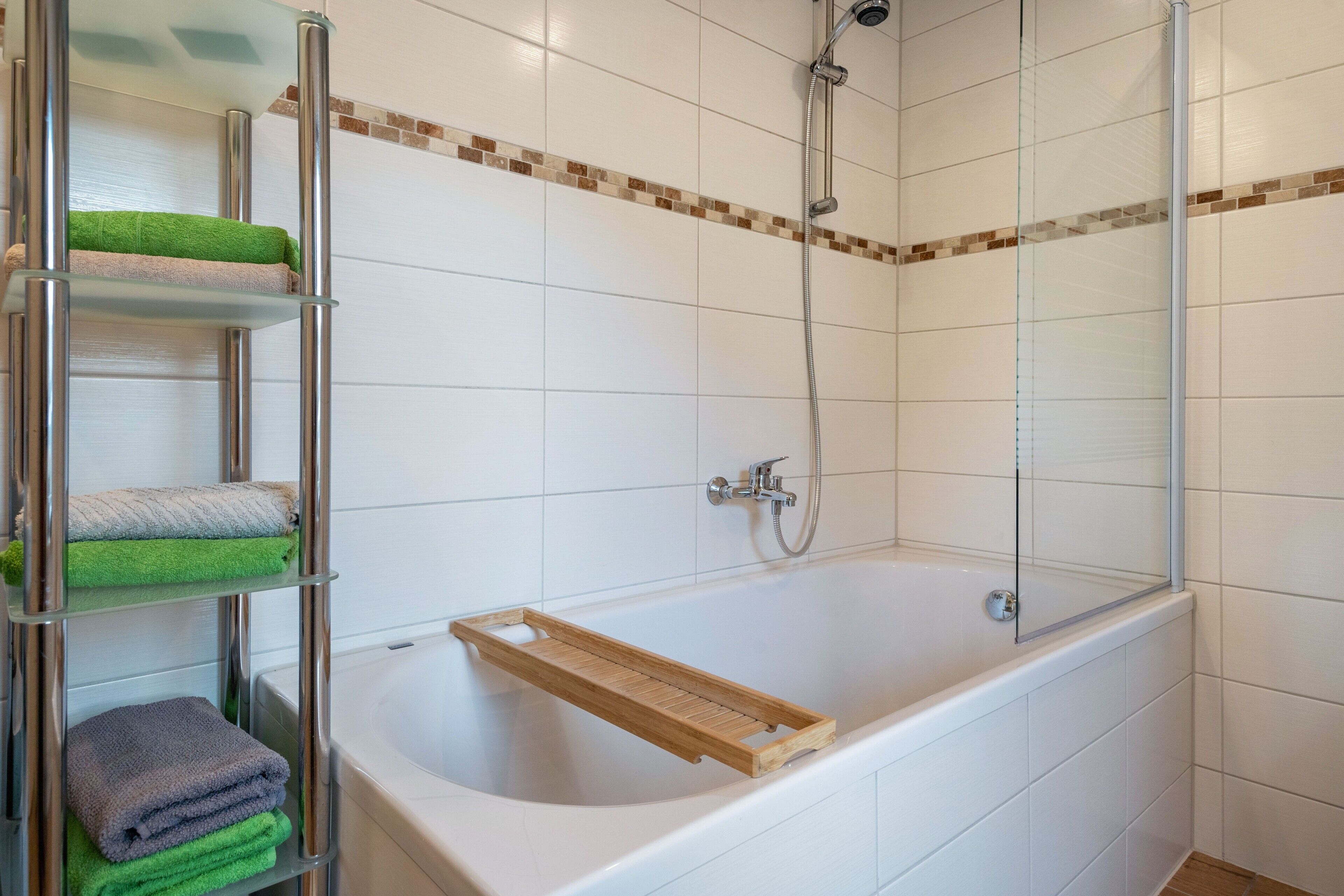 A modern bathroom with a glass shower enclosure, a white bathtub, and a metal towel rack with folded towels.