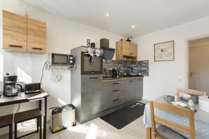 Eine kleine Küche mit Mikrowelle, Toaster und Kaffeemaschine, ein Essbereich mit Tisch und Stühlen sowie ein kleiner Mülleimer.