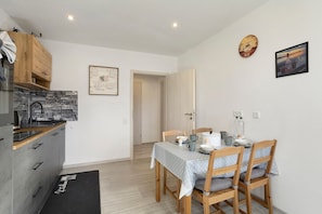 Uma cozinha compacta com painel de pedra, uma mesa de jantar com cadeiras e um relógio na parede.