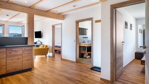 A spacious room with wooden beams, a kitchen area, a yellow chair, and a large window.