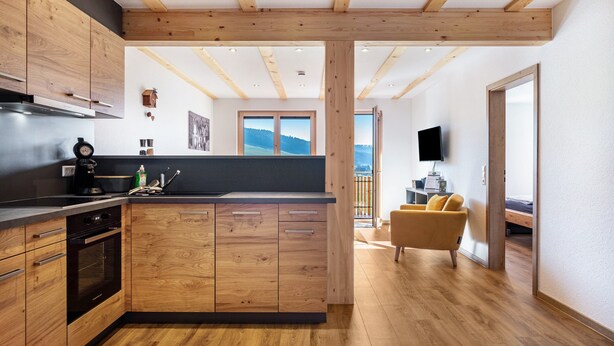 A modern kitchen with wooden cabinets, a central island, and a dining area with a sofa.