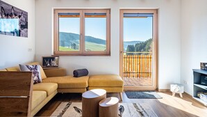 A modern living room with a sofa, wooden beams, a wooden side table, and a view through large windows.
