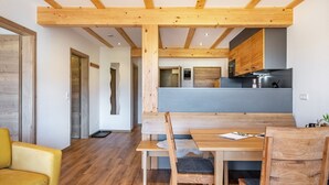 A modern interior with wooden beams, a dining table, chairs, a sofa, and a kitchen area.