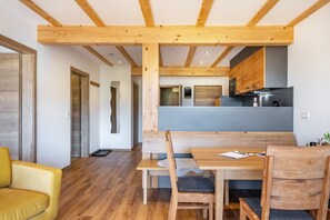 Un interior moderno con vigas de madera, una mesa de comedor, sillas, un sofá y una zona de cocina.