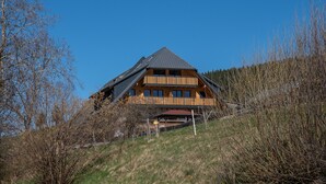 Een groot houten huis met een steil dak, omringd door bomen en gras.