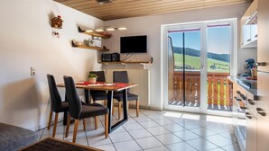 Een eethoek met een tafel, stoelen, een televisie en uitzicht door een schuifdeur.