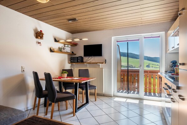 A dining area with a table, chairs, a television, and a view through a sliding glass door.